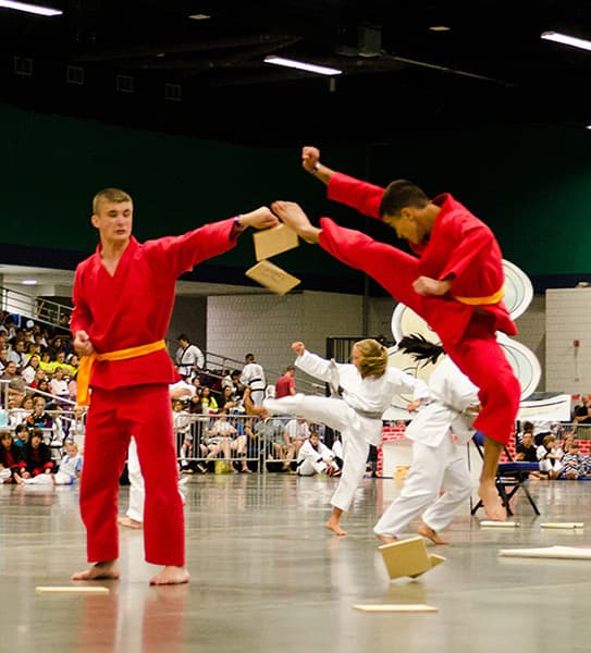 Competitors in red costumes performing a jumping board break as part of a Creativity routine.