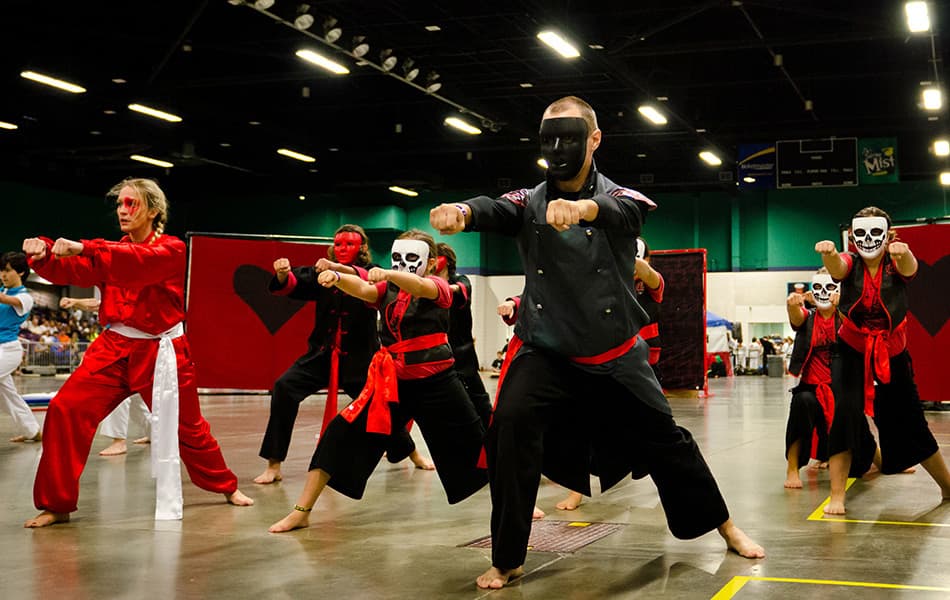 A large team in matching red-and-black masked costumes performing a synchronized choreographed routine.