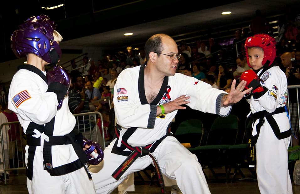 A center judge standing directly between two young sparring competitors before the start of a match.