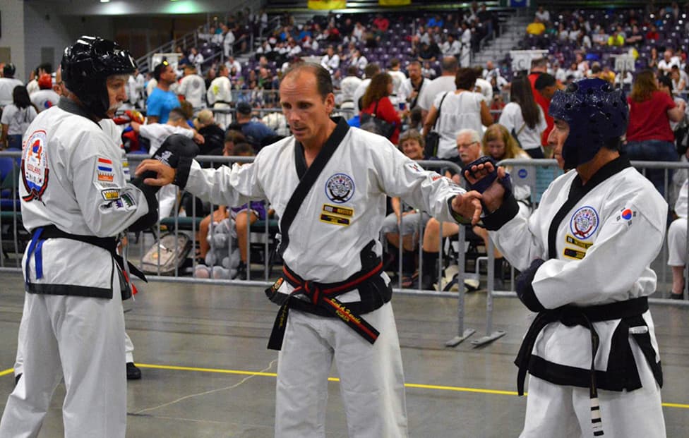 A center judge with arms raised, actively managing two adult competitors in the ring.