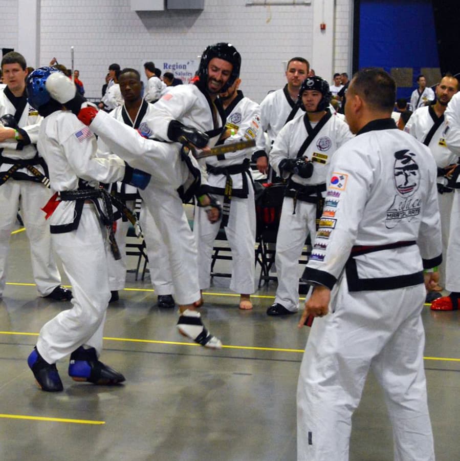A live team sparring match with teammates and a coach watching closely from just outside the ring.