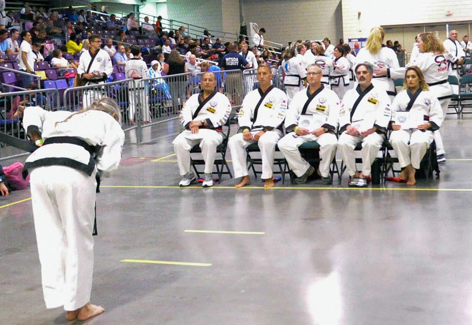 A center judge and row of corner judges seated ringside as a competitor bows before them.